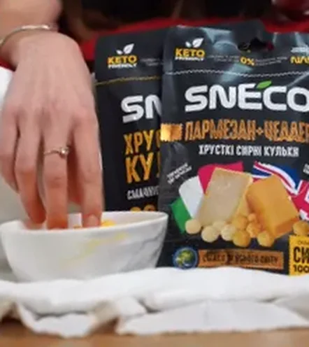 Рука бере сирні кульки snEco з миски поруч із пачками